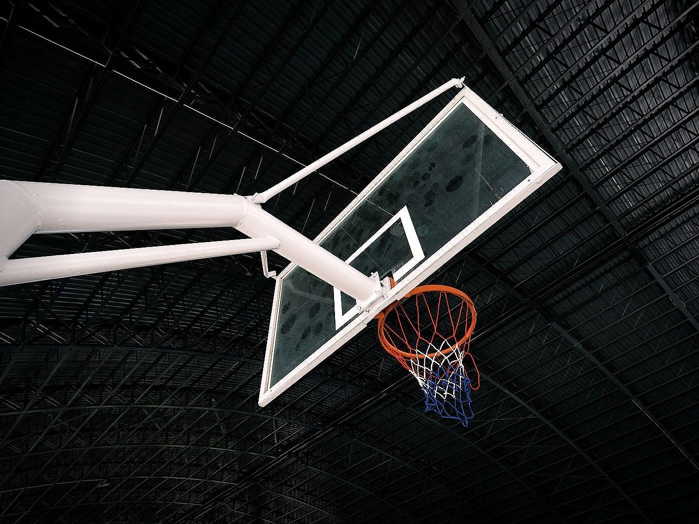 A basketball rim, net and backboard photographed from below in an empty sports hall