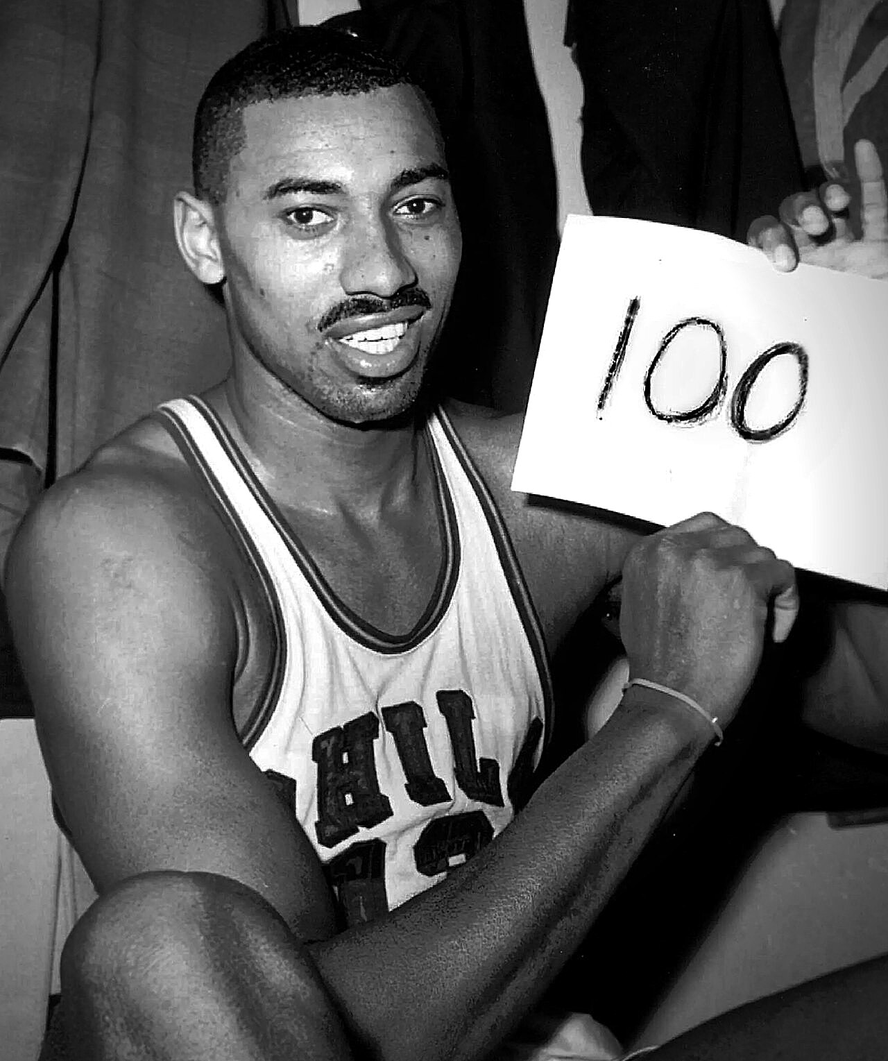 Wilt Chamberlain in a Philadelphia Warriors jersey holding a sheet of paper reading 100